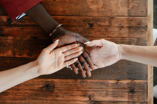 Three individuals of different ethnicities gently holding hands on a wooden surface, symbolizing support and unity.