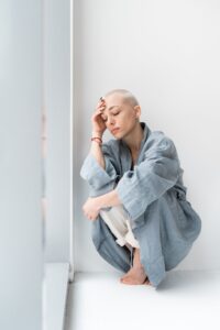 A person sitting on the floor against a white wall, wearing a blue robe and a thoughtful expression, embodying a moment of introspection or concern.