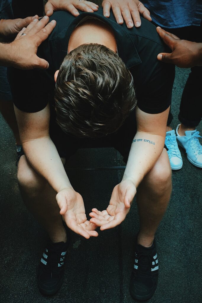 Young man in recovery hands out supported by others with hands on their back